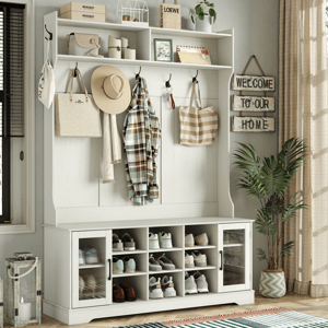 Entryway storage unit with shelves, hooks, and cubbies for shoes. Features hats, bags, a plaid shirt, and decor items like candles and plants. A sign reads \“Welcome to Our Home,\“ and there's a lantern and potted plant nearby.