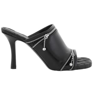 Black high-heeled mule with zipper details and decorative charms on the leather upper and a quilted sole.