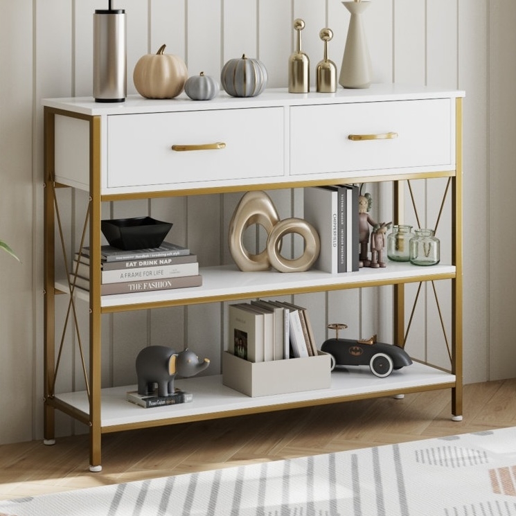A gold and white console table with two drawers, featuring decorative pumpkins, vases, books, a toy elephant, and a toy car.