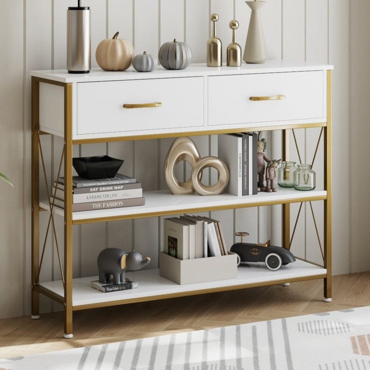 A gold and white console table with two drawers, featuring decorative pumpkins, vases, books, a toy elephant, and a toy car.