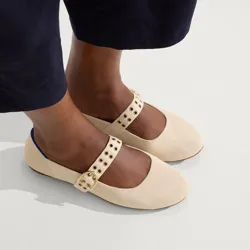 A pair of beige Mary Jane shoes with gold buckles and eyelet details is worn with dark pants.