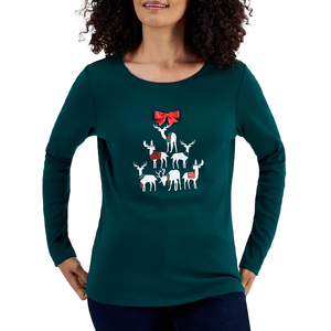 A woman is wearing a green long-sleeve top featuring a design of reindeer arranged in a tree-like formation with a prominent red bow above them.