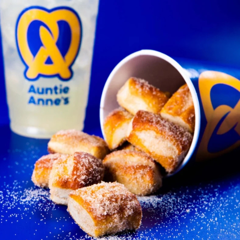Auntie Anne's cup of lemonade and a container of sugar-coated pretzel bites are on display against a blue background.