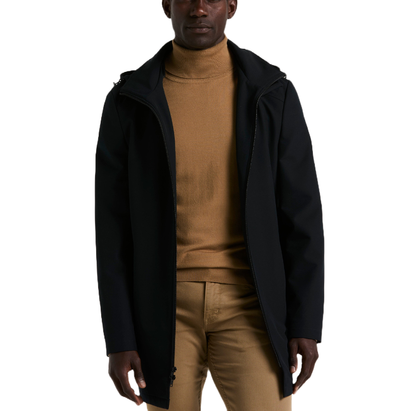 A man wears a black coat over a tan turtleneck and tan pants.