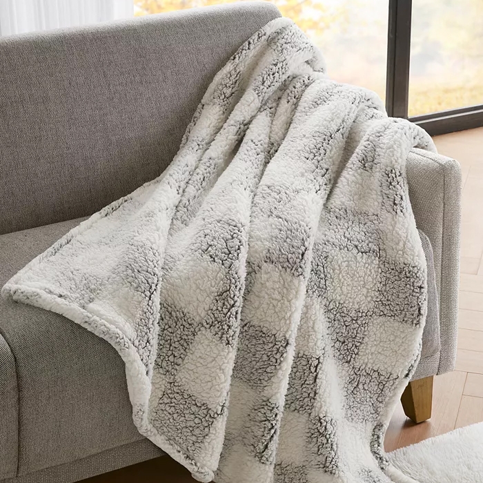 A soft, checkered-patterned blanket draped over a light gray sofa near a window.
