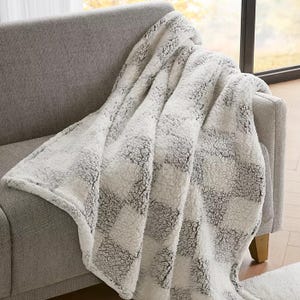 A soft, checkered-patterned blanket draped over a light gray sofa near a window.