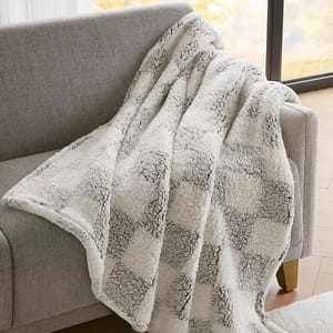 A soft, checkered-patterned blanket draped over a light gray sofa near a window.