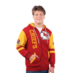 A man is wearing a red and yellow full-zip hooded sweatshirt with the \“CHIEFS\“ logo and team's emblem on the front.