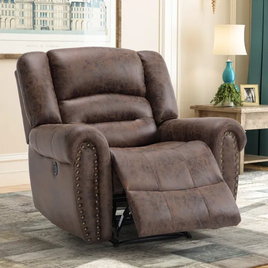 A brown leather recliner with nailhead trim is positioned in a living room setting, featuring a side table with a lamp and decorative items.