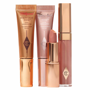 Four Charlotte Tilbury makeup products including two highlighter wands in different shades and two lipsticks in complementary hues, featuring rose gold and clear packaging with brand logos.