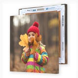 A canvas print shows a child in a colorful coat and red beanie holding large autumn leaves, with another identical canvas print partially visible behind it.