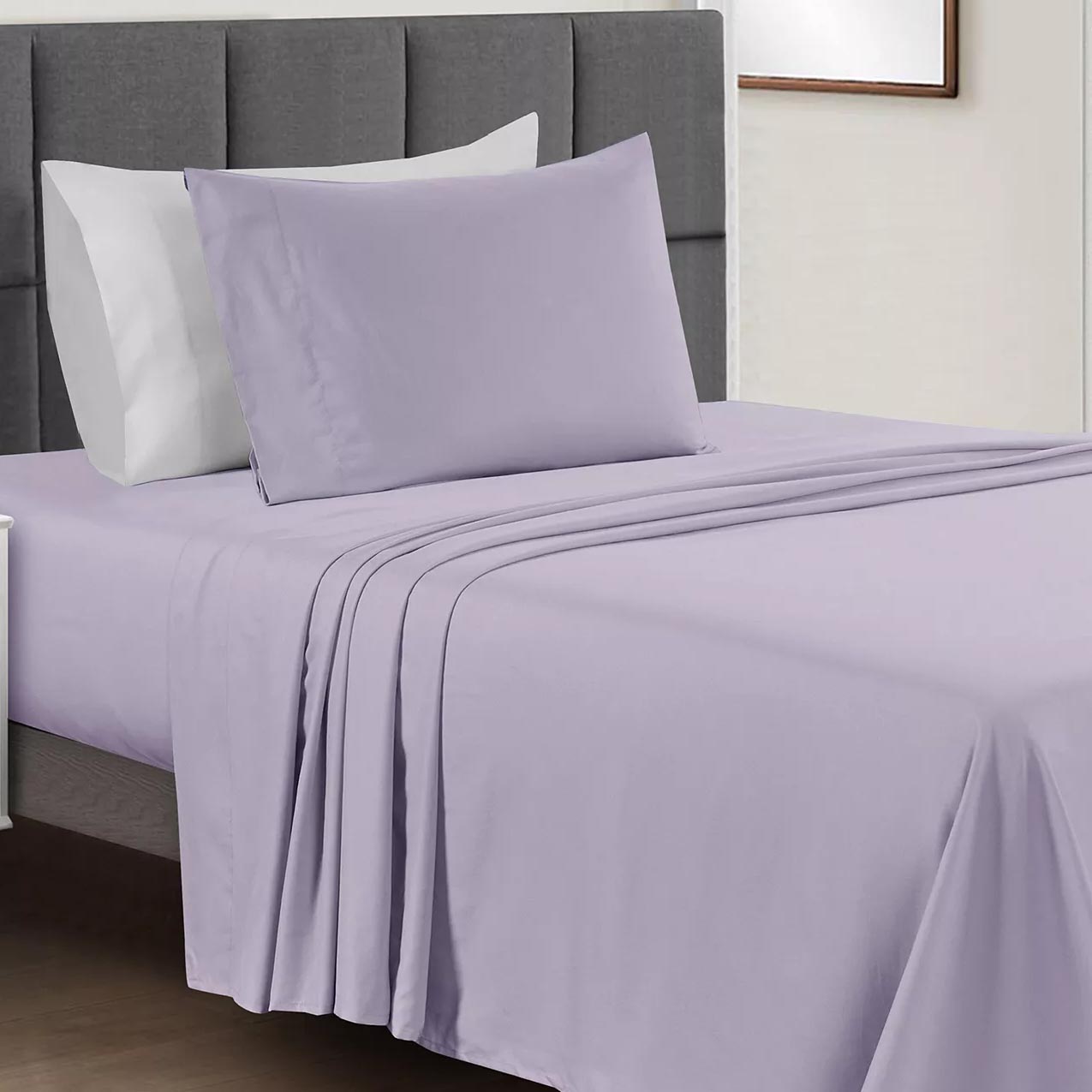 A bed is made with a light purple sheet set, including a fitted sheet, flat sheet, and pillowcases, accompanied by a grey upholstered headboard.