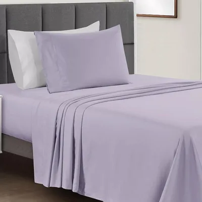 A bed is made with a light purple sheet set, including a fitted sheet, flat sheet, and pillowcases, accompanied by a grey upholstered headboard.