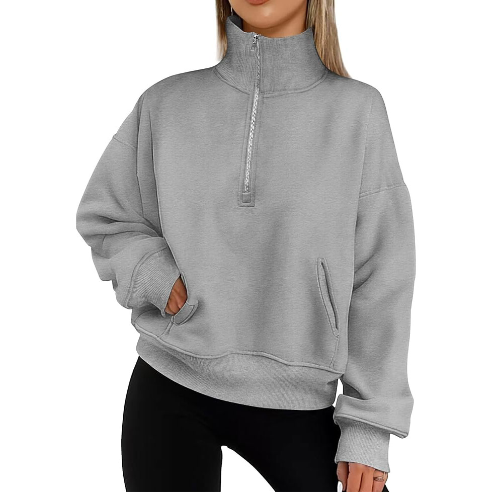A gray oversized half-zip sweatshirt with a high collar, featuring dropped shoulders, ribbed cuffs, and a roomy fit. It has a large pocket on the front and is paired with black leggings.