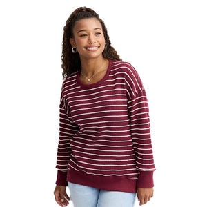 A woman is wearing a maroon sweater with white horizontal stripes paired with light blue jeans.