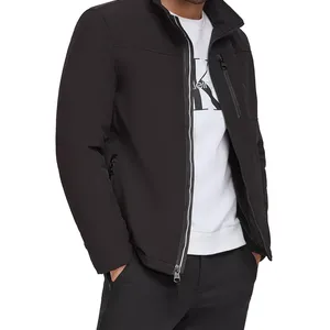 A man is wearing a black zip-up jacket with a stand collar over a white shirt and black pants, featuring zippered pockets.