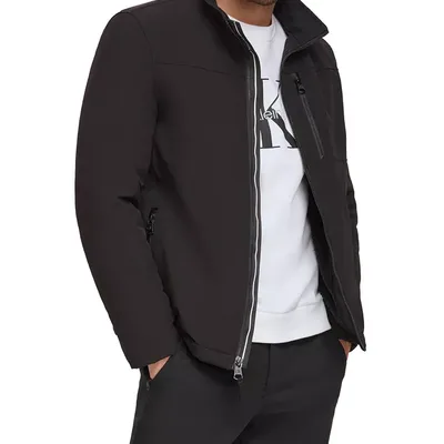 A man is wearing a black zip-up jacket with a stand collar over a white shirt and black pants, featuring zippered pockets.