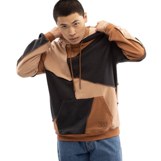 The UGG All-Gender Piecework Hoodie features a patchwork design with black, brown, and beige fabric, a front pocket, and a hood with drawstrings. It has a casual, relaxed fit suitable for any gender.