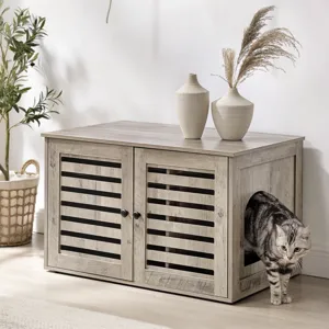A wooden pet furniture with louvered doors and a side entrance is shown, accompanied by decorative vases on top. A cat is emerging from the entrance. The setting includes a leafy plant in a basket and a cozy beige sofa.