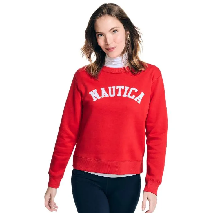 A red Nautica sweatshirt with long sleeves and a crew neck, featuring the brand name \“NAUTICA\“ in white, capitalized arch lettering across the chest. The wearer also has a white turtleneck underneath and is paired with dark pants.