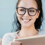 A person with glasses is smiling while holding a tablet.
