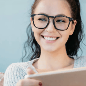 A person with glasses is smiling while holding a tablet.