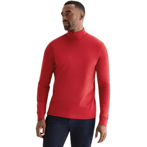 A man is wearing a red turtleneck sweater and dark blue jeans, standing against a plain background.