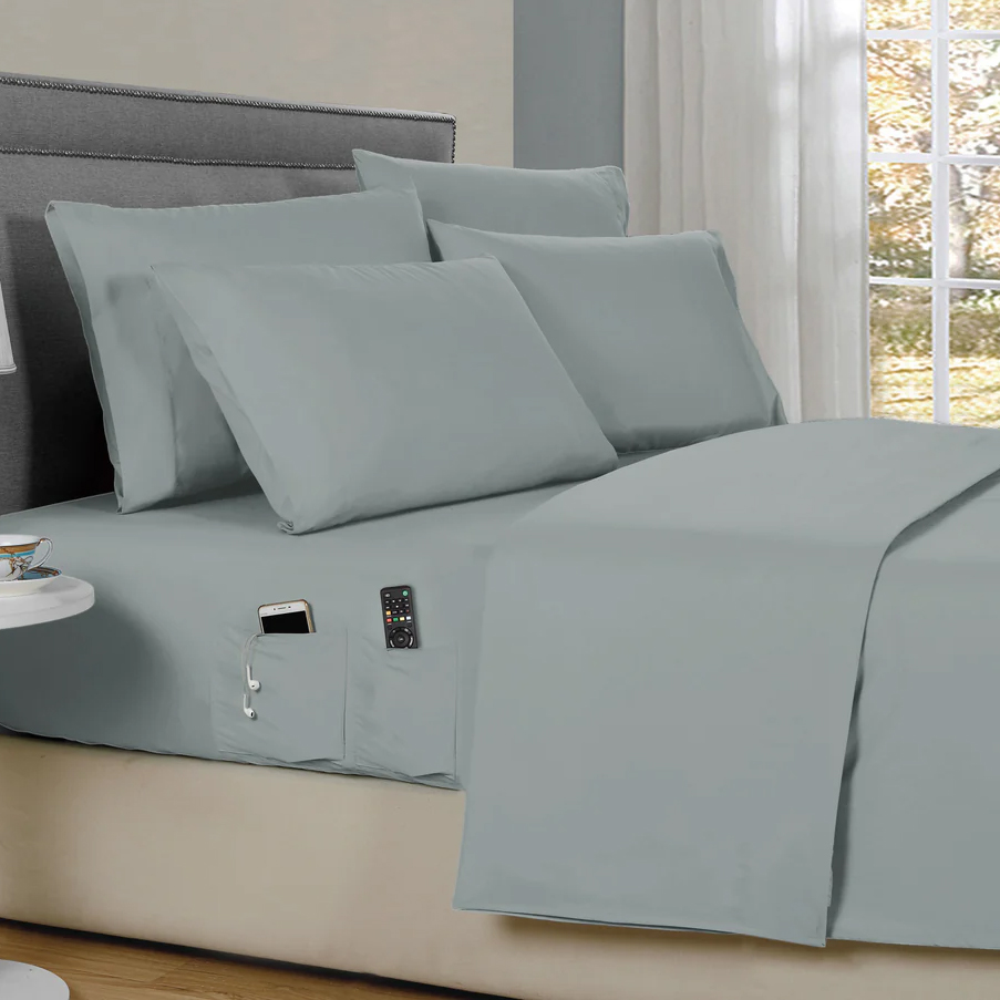 A bed with light gray sheets features pockets on the side for storing a phone, remote, and earphones.
