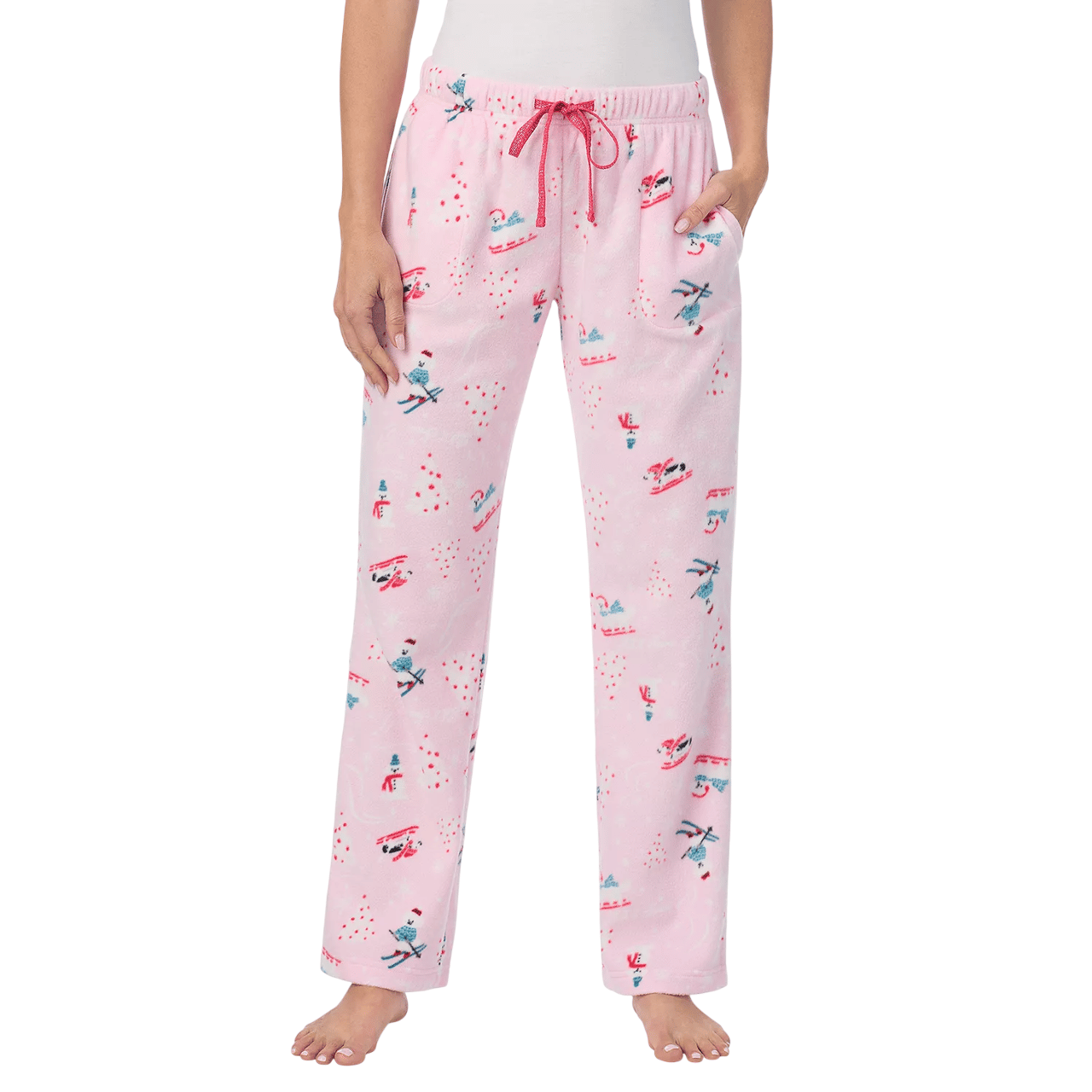 Pink pajama pants with a winter-themed print, featuring snowmen, sleds, and skiing motifs. Decorated with a red drawstring and pockets, worn by a person standing barefoot.