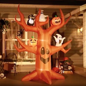 An inflatable Halloween tree decoration with pumpkins, ghosts, and an owl adorns a house's front porch.