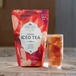 Harney & Sons Fresh Brew Iced Tea Blood Orange Herbal Infusion, featuring 15 two-quart tea bags, along with a glass of orange-infused iced tea on a wooden surface.