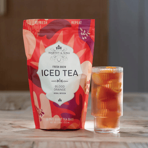 Harney & Sons Fresh Brew Iced Tea Blood Orange Herbal Infusion, featuring 15 two-quart tea bags, along with a glass of orange-infused iced tea on a wooden surface.