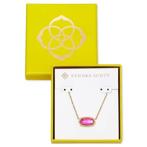 A Kendra Scott necklace with a pink oval-shaped pendant set in a gold chain, packaged in a yellow box with a floral logo.
