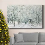 Canvas art depicting a snowy forest scene with a house surrounded by trees, hung above a gray sofa. A decorated Christmas tree with gold baubles stands nearby.