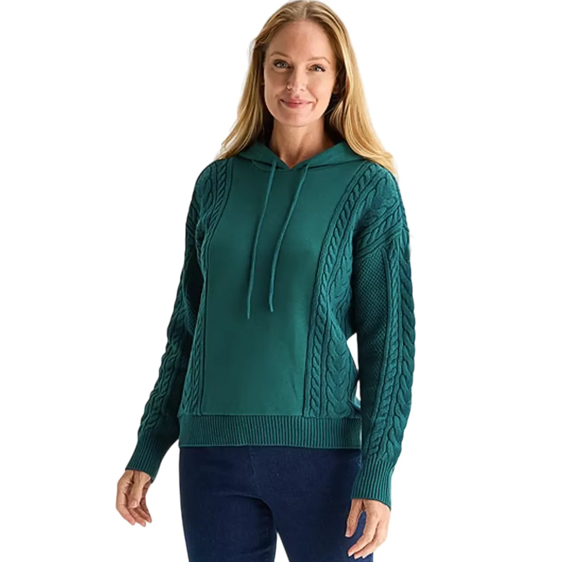 A woman is wearing a teal hooded sweater with cable knit detailing on the sleeves and sides, paired with dark blue jeans.