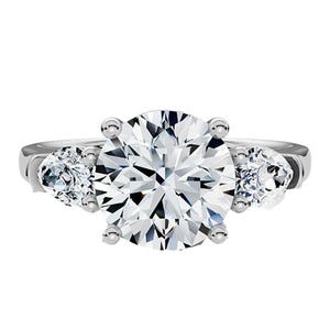 A lab-grown diamond ring features a large round center stone flanked by two smaller side diamonds, set in a sleek, polished band.
