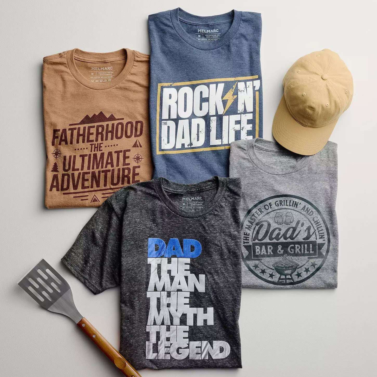 Four Father's Day T-shirts and a cap are displayed: a brown tee with \“Fatherhood the Ultimate Adventure,\“ a blue tee with \“Rock 'N the Dad Life,\“ a grey tee with \“Dad's Bar & Grill,\“ and a dark grey tee with \“Dad The Man The Myth The Legend,\“ plus a BBQ spatula.