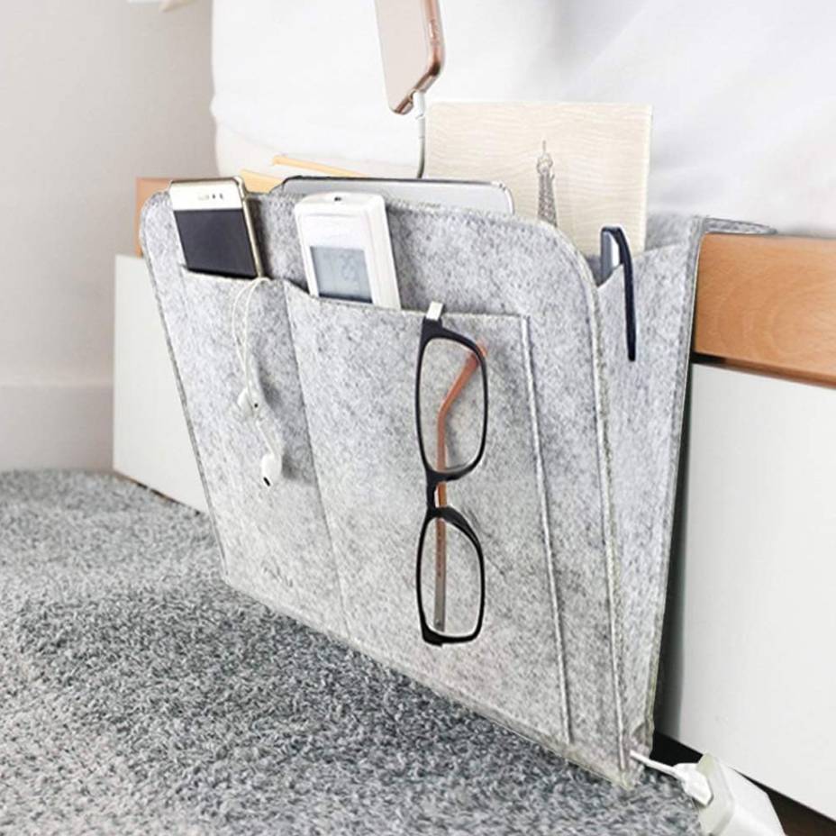 A felt bedside caddy holding a book, glasses, smartphones, and a remote control.