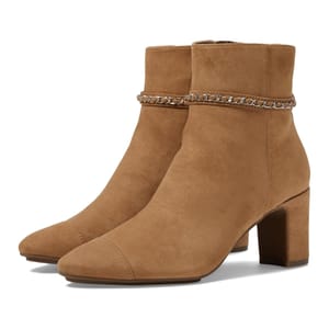 Anne Klein Suri Boots are tan suede ankle boots with block heels and a decorative chain detail around the ankle. They feature a sleek, simple design for stylish wear.