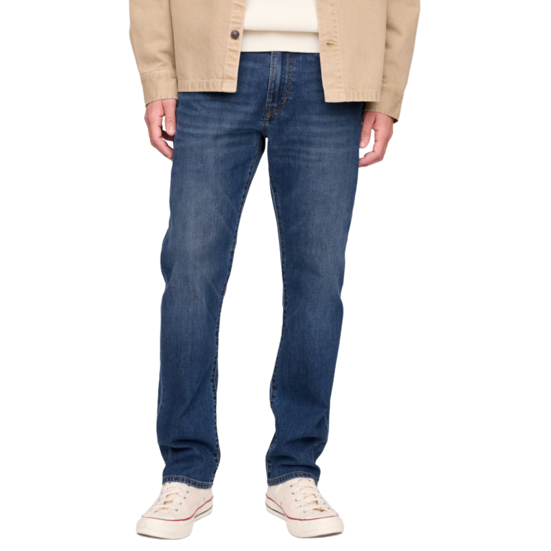 Male model wearing straight-leg blue jeans, white sneakers, and a beige jacket over a white shirt.