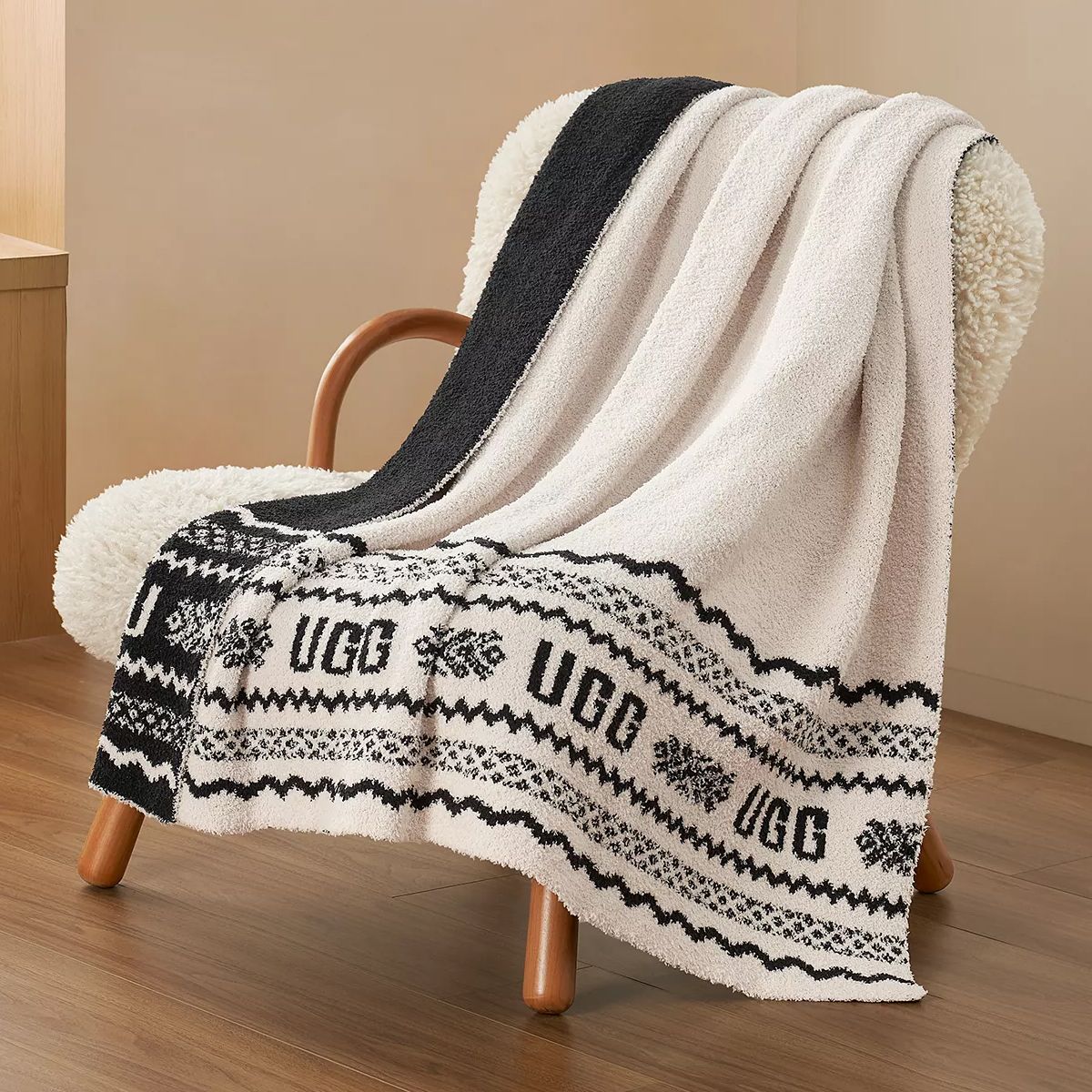 A black and white UGG blanket with a Scandinavian pattern is draped over a cozy chair with wooden legs.