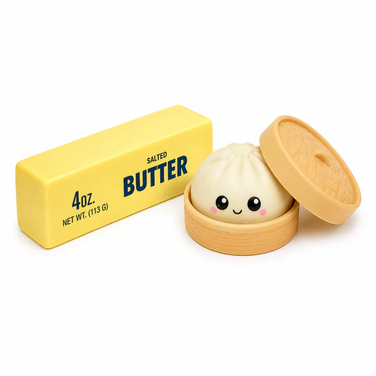 A stick of salted butter labeled \“4 oz.\“ is next to a cute dumpling toy with a smiling face, placed inside a small bamboo steamer.