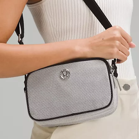 A person is carrying a small black and white crossbody bag with a patterned design and a logo emblem on the front.