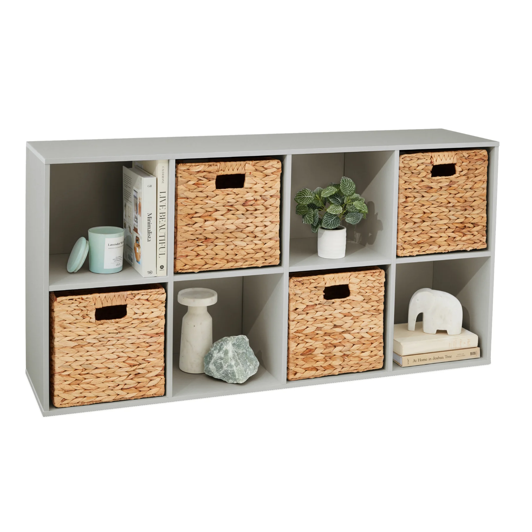 A cube organizer with six compartments includes four woven baskets, a small potted plant, books, and decorative items like a candle, vase, and figurine.
