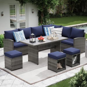Outdoor patio set featuring a sectional sofa with navy cushions, a rectangular table, and matching stools on a tiled patio. Decorative pillows, a lantern, and a tray with snacks are on the table, set in a garden with a pool in the background.