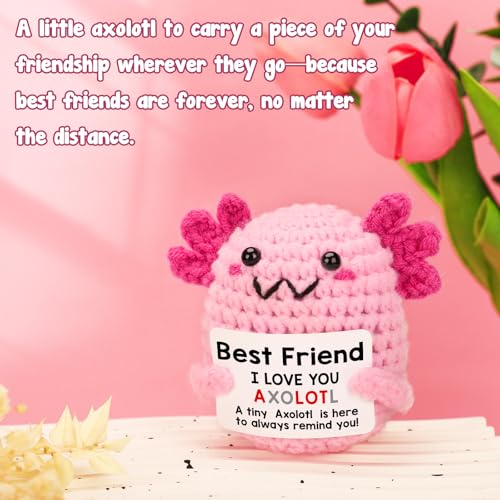 A pink crocheted axolotl holding a \“Best Friend\“ sign with a friendship message, accompanied by pink tulips in the background.