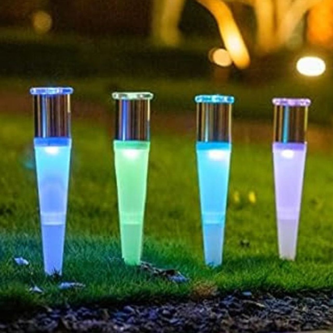 Four solar-powered LED garden lights with a tapered design, glowing in blue and green shades, illuminate a lawn.