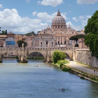 A view of St. Peter's Basilica in Vatican City with the Tiber River and a bridge in the foreground.