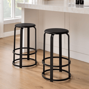 Two black metal bar stools with round seats are placed near a white marble countertop in a modern kitchen setting, featuring wood flooring, a potted plant, and wall art.