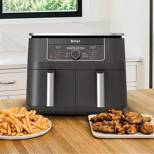 A Ninja air fryer on a kitchen counter with a plate of french fries and chicken wings beside it.
